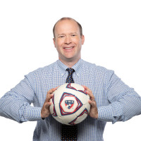 Dan Hunt smiles while holding an FC Dallas soccer ball.