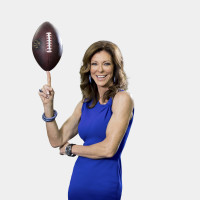 Charlotte Jones wears a bright blue dress and smiles while balancing a football on her pointer finger.